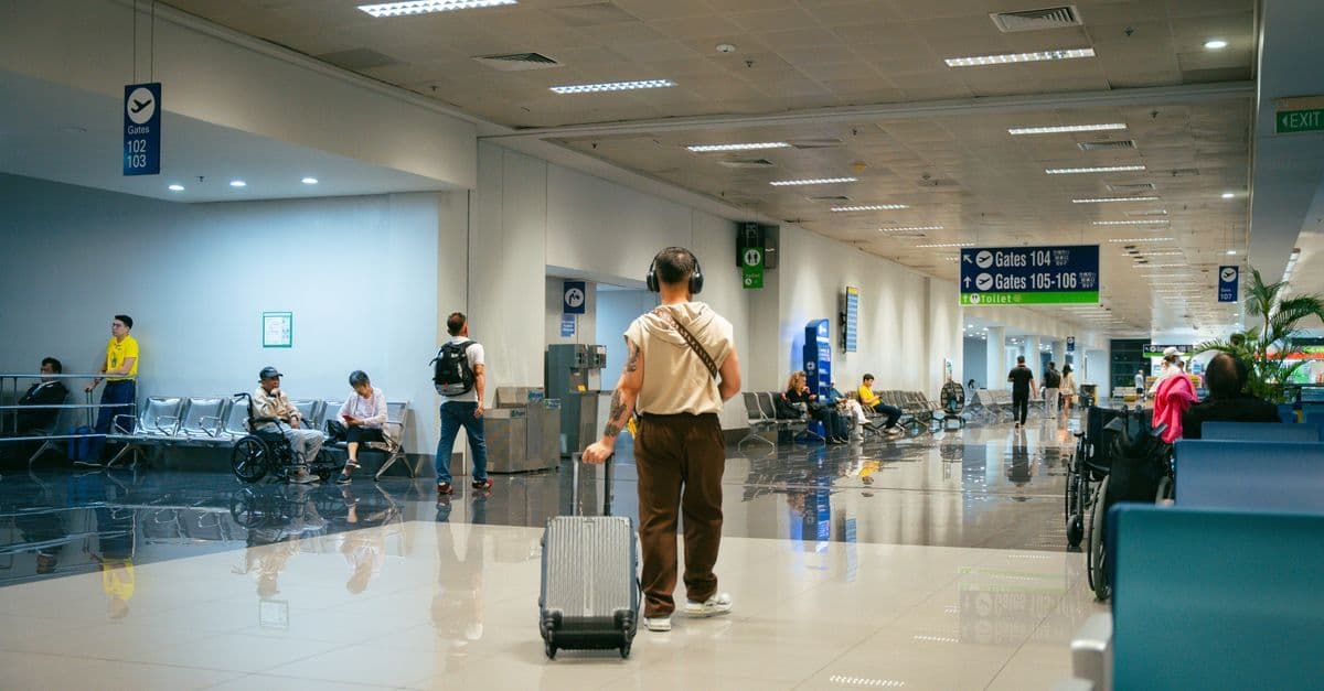 空港の広い通路を、スーツケースを引く旅行者が搭乗ゲートへ向かって歩いている。