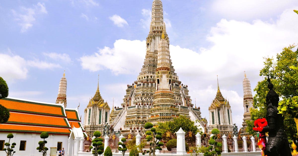 Ornate Wat Arun temple silhouette against clear blue sky, an essential place to visit in Thailand