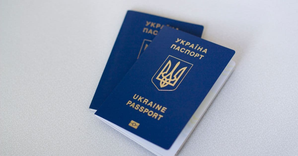 Two blue Ukrainian passports with gold trident emblems stacked on a light textured surface.