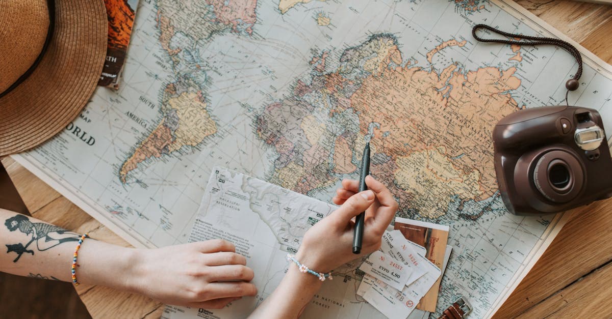 Top view of hands planning a trip with a map, camera, and essential travel checklist items.