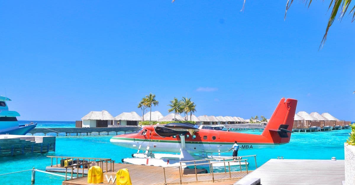 Wasserflugzeug an einem Steg vor türkisfarbenem Meer und Overwater-Bungalows unter klarem Himmel auf den Malediven.
