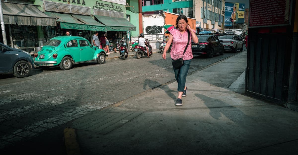 Mujer caminando frente a edificios coloridos y autos vintage en Trujillo, Perú, conectada con una eSIM regional.