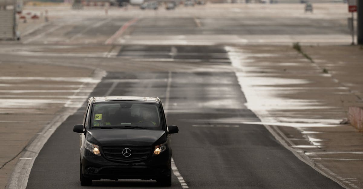 Fourgon noir sur le tarmac pluvieux de l'aéroport de Madrid, avec des avions en arrière-plan.