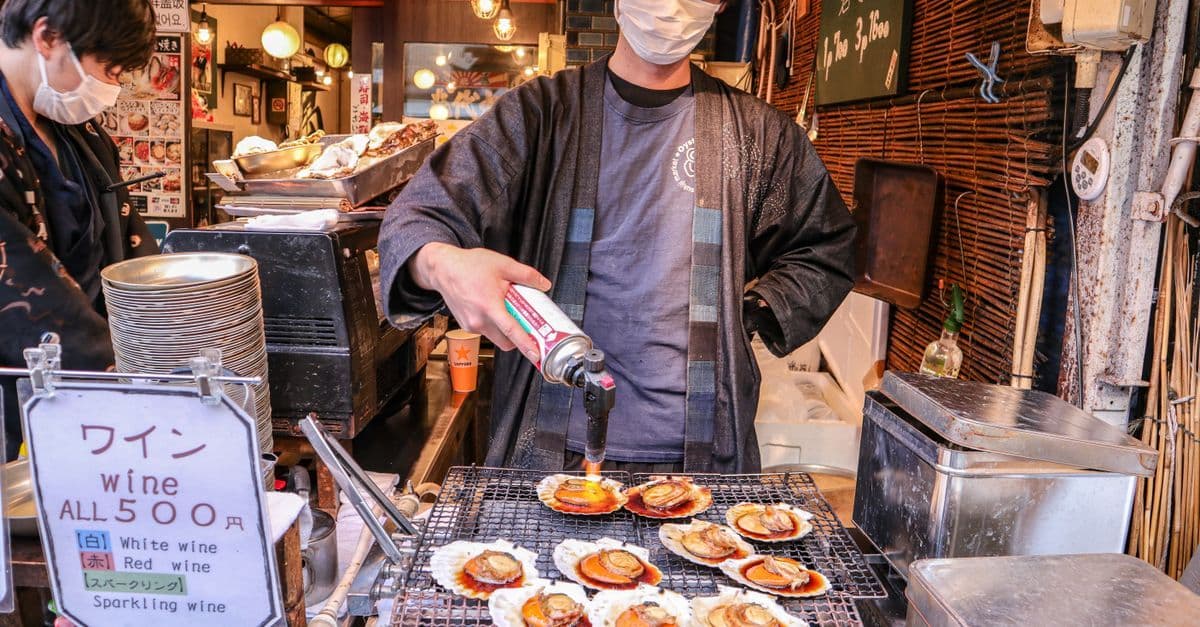Chef using a flame torch to grill fresh clams at a tokyo grill street food stall