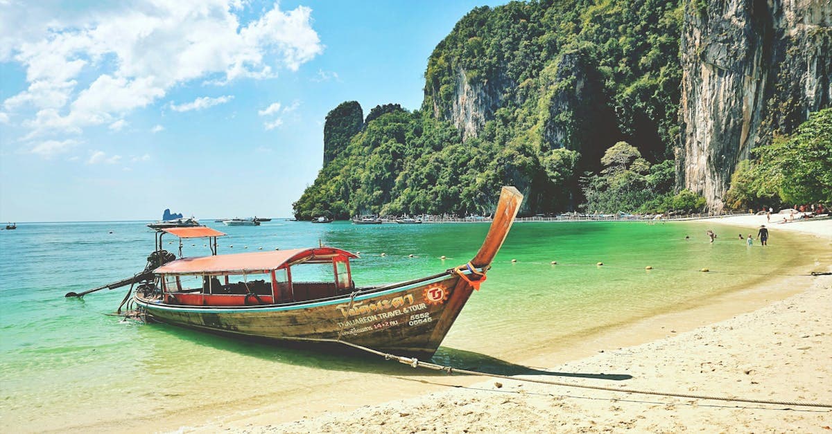 Longtail boat moored beside dramatic limestone cliffs on a tranquil Krabi beach in Thailand.