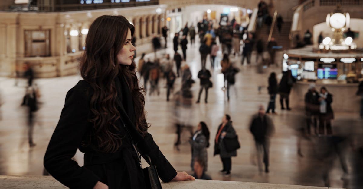 Woman relaxing with her backpack in a golden wheat field, packing light for solo female travel.
Start with the tech layer, not the clothing pile. An unlocked smartphone with an eSIM installed before departure (setup is covered earlier in this guide) is the non-negotiable anchor. Pair it with a portable battery pack of at least 10,000 mAh: at that capacity, most modern phones fully recharge twice. Add a door-stop alarm and a personal safety alarm. Both add deterrent capability with negligible weight and pack flat in a toiletry bag.
Documents require a backup system. Carry physical copies of your passport, visa, travel insurance card, and first-night hotel address in a separate bag from the originals. A stolen bag should not leave you unable to prove your identity or locate your accommodation.
Data is a real budget line item. US carrier roaming for a two-week trip can run above $350, while regional eSIM plans cost a fraction of that figure. The specific daily rates were covered in the connectivity section above. Budget for data alongside flights and accommodation rather than treating it as an afterthought.
For Morocco, Abu Dhabi, and parts of Southeast Asia, pack at least two modest clothing options. Loose linen trousers and a lightweight long-sleeved layer meet conservative dress requirements and double as practical packable pieces in any climate.
First aid basics: prescription medications in original packaging (a customs requirement in most countries), blister care, and rehydration salts for warm-weather destinations. An RFID-blocking wallet and a low-profile money belt earn their weight at crowded markets and transit hubs.
Packing light is a safety strategy, not just a convenience. A manageable carry-on means faster exits at arrivals, no checked-luggage delay, and the freedom to move quickly when the situation calls for it.
How Do I Meet People When Travelling Solo as a Woman?
![Woman travelling solo observing the vibrant crowd inside Grand Central Terminal, New York City