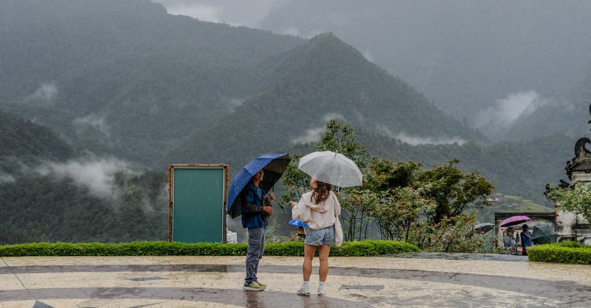 Couple sous parapluies lors d'une journée pluvieuse en montagne thaïlandaise illustrant les mois à éviter pour la météo thaïlande