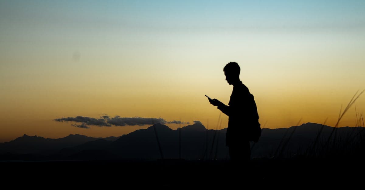 Silhueta de viajante usando smartphone ao pôr do sol com montanhas ao fundo, sem roaming caro