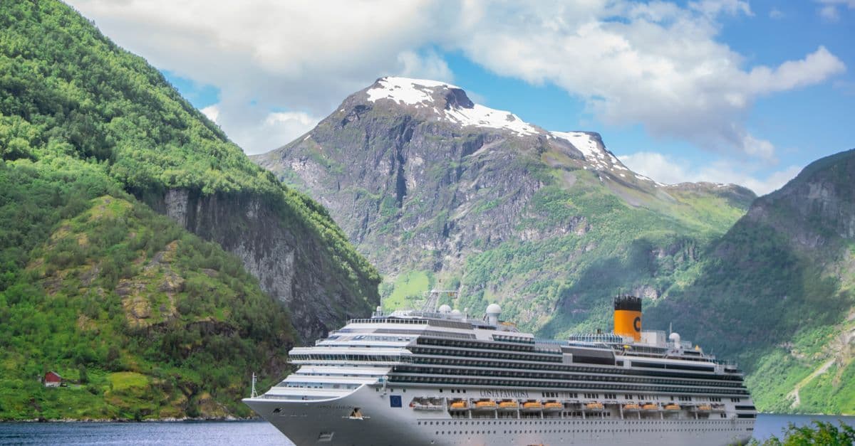 A large cruise ship navigates the glassy waters of Geiranger Fjord, encircled by towering Norwegian mountains