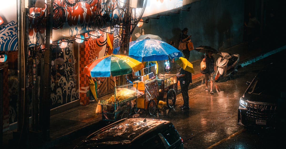 Colourful street stalls under umbrellas on a rainy Bangkok night serving crab omelette and sticky rice