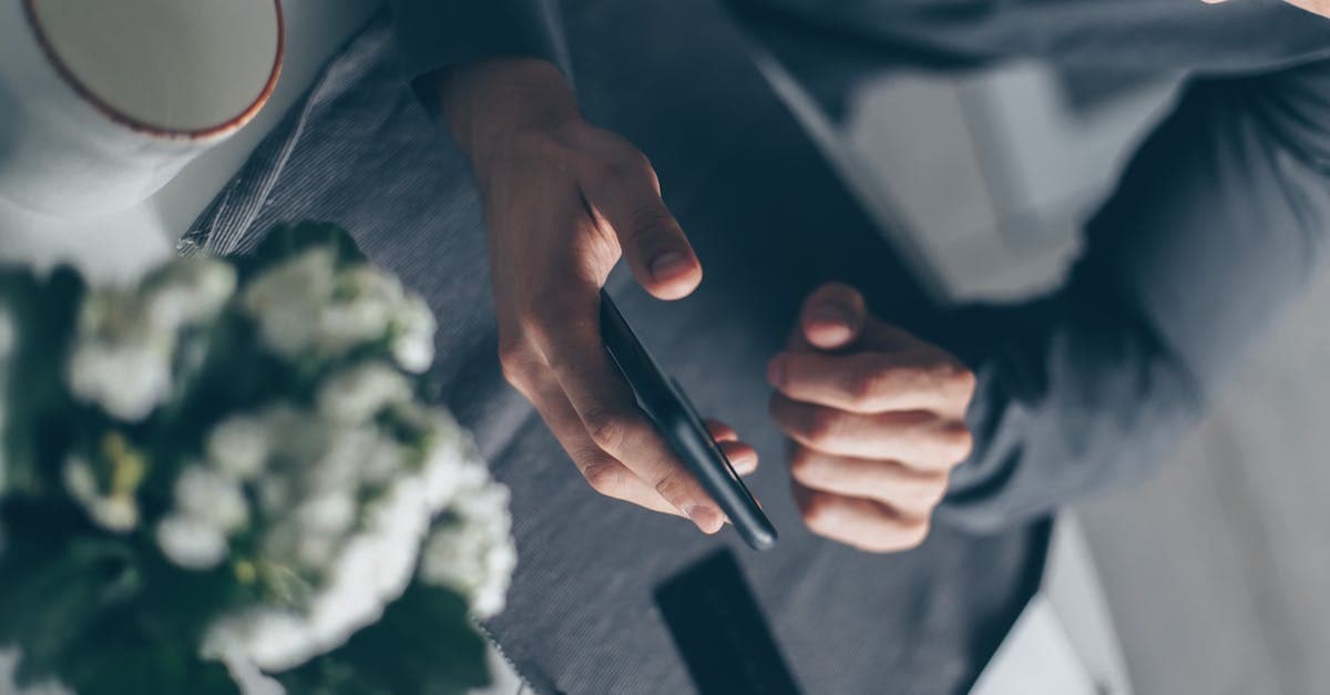 Overhead close-up of hands holding a phone indoors, beside a coffee cup and flowers on a desk.