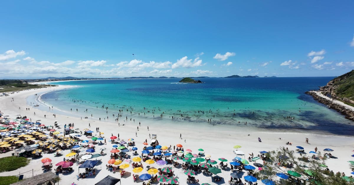 Vista aérea de praia brasileira com guarda-sóis coloridos, comparando a melhor época para o verão na europa