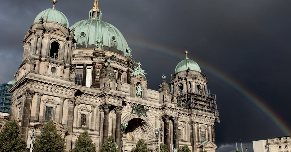 Berlin Cathedral with a rainbow under an overcast sky, capturing its historical architecture.