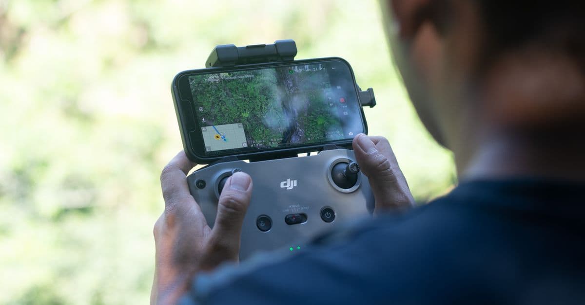 Pilota con telecomando del drone e smartphone che utilizza la piattaforma d-flight per monitorare il volo