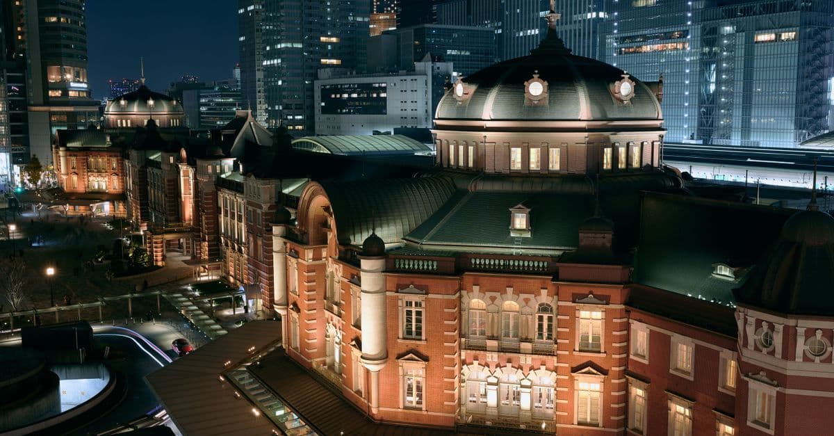 La stazione di Tokyo di notte, architettura storica dell'era Meiji immersa tra i grattacieli moderni.