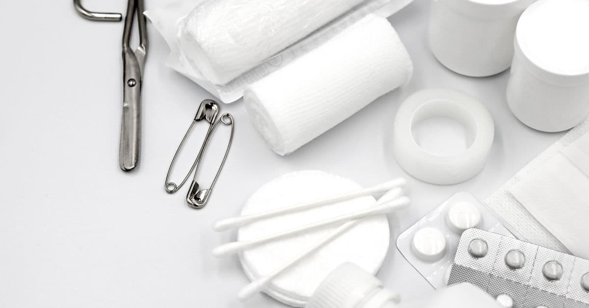 Verbandsmaterial, Schere, Sicherheitsnadeln, Wattestäbchen und Tabletten liegen als mögliche Inhalte einer Reiseapotheke bereit.