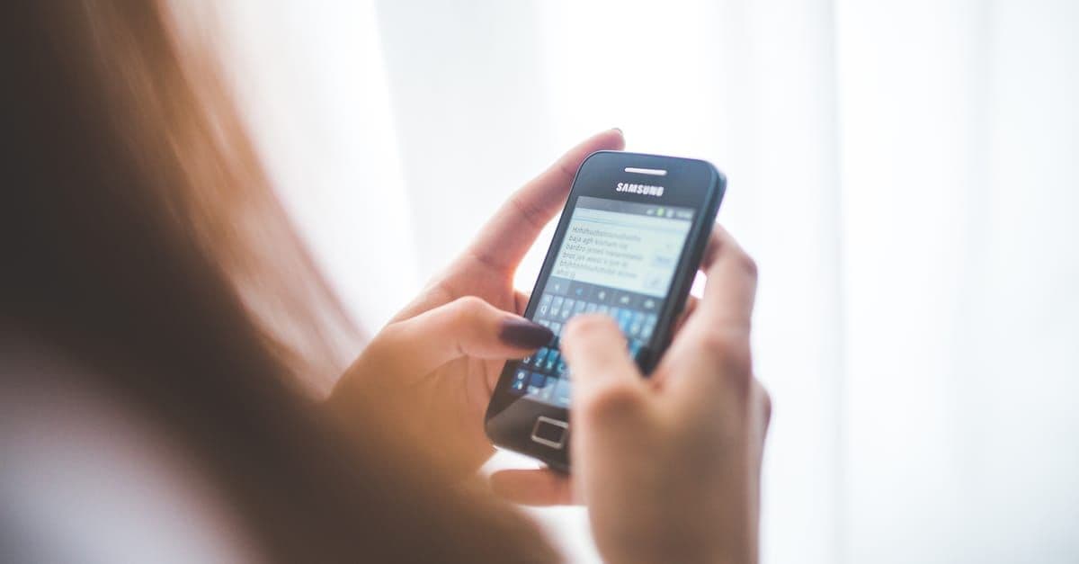 Junge Frau tippt auf ihrem Samsung-Smartphone zu Hause und synchronisiert Daten über Samsung Cloud.