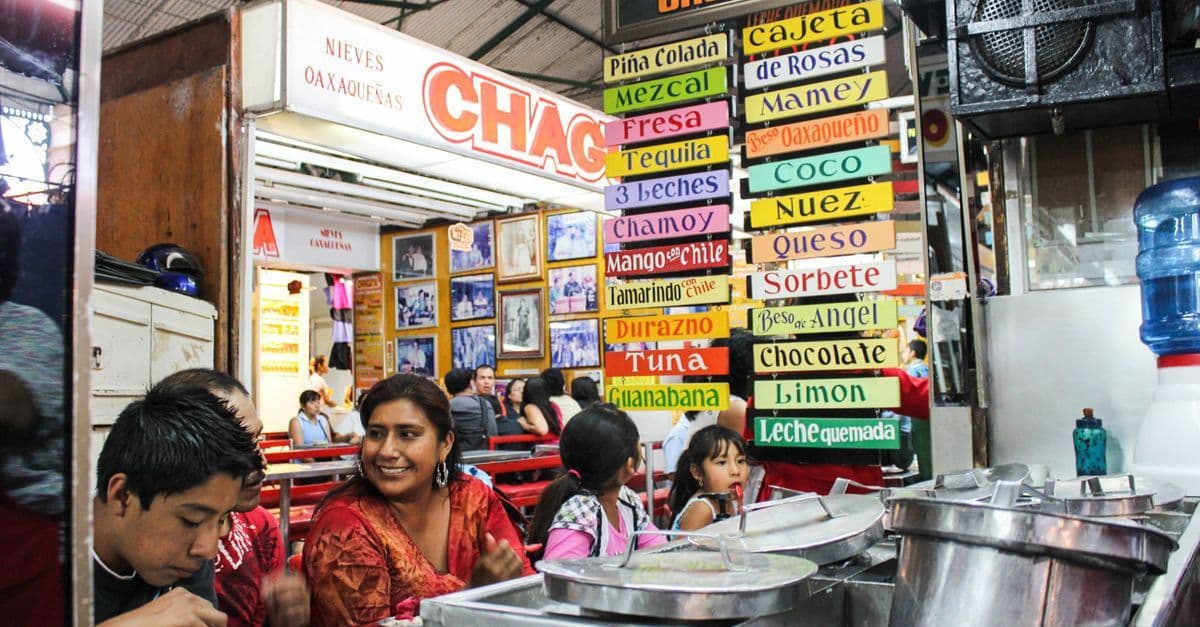 Customers enjoying Mexican ice cream at a lively Oaxacan shop filled with colorful handwritten signs.