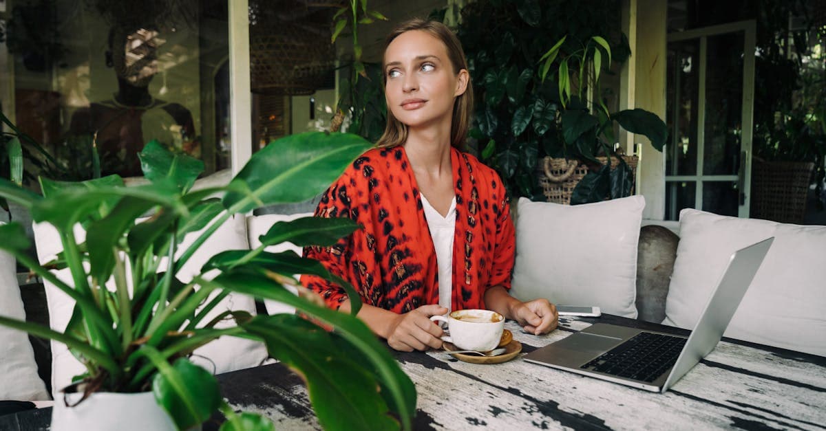 Woman enjoying coffee while working remotely indoors surrounded by lush tropical Bali greenery