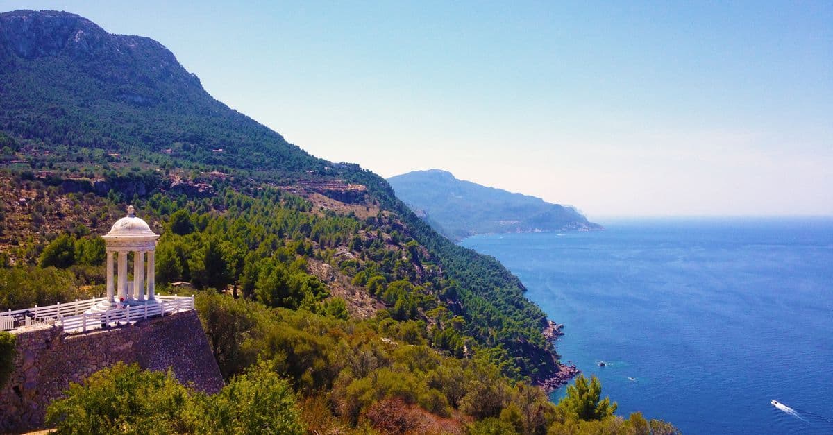 Traumhafte Mallorca Urlaub Aussicht mit Pergola, üppigem Grün und azurblauem Meer an der Küste.