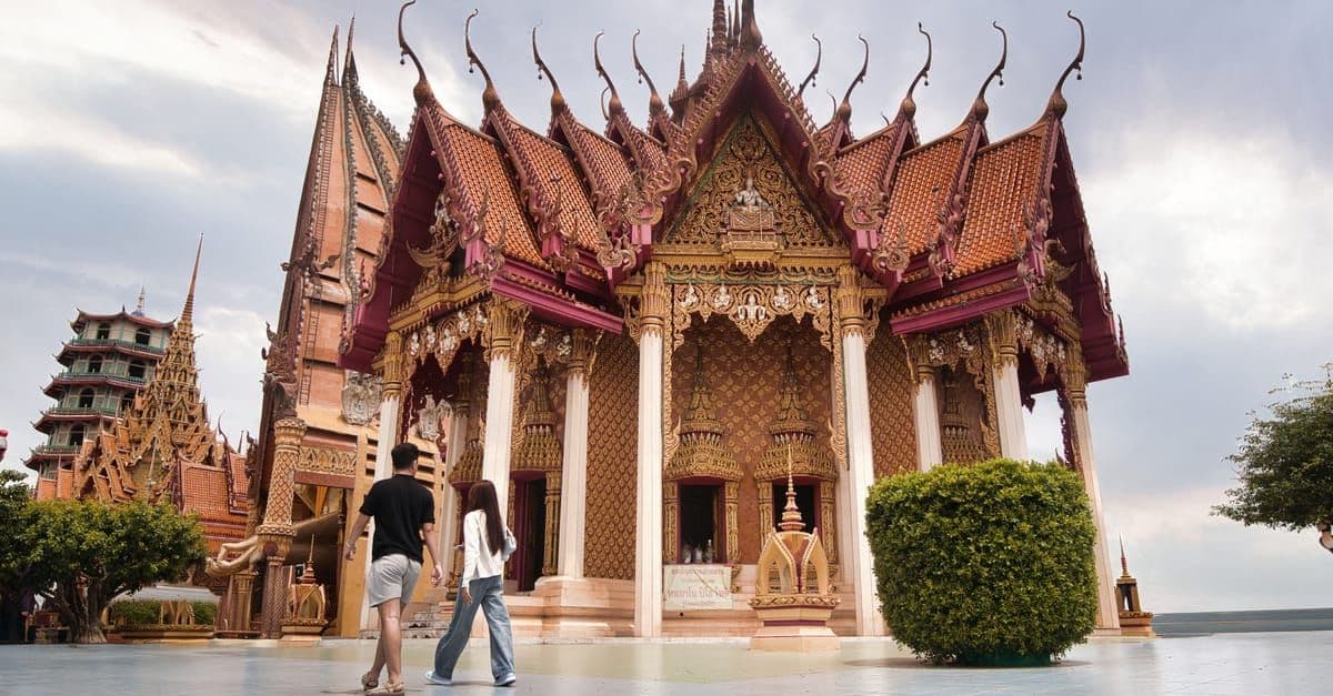 Couple strolling past an ornately decorated Thai temple, capturing romance in Thailand holiday packages for couples.