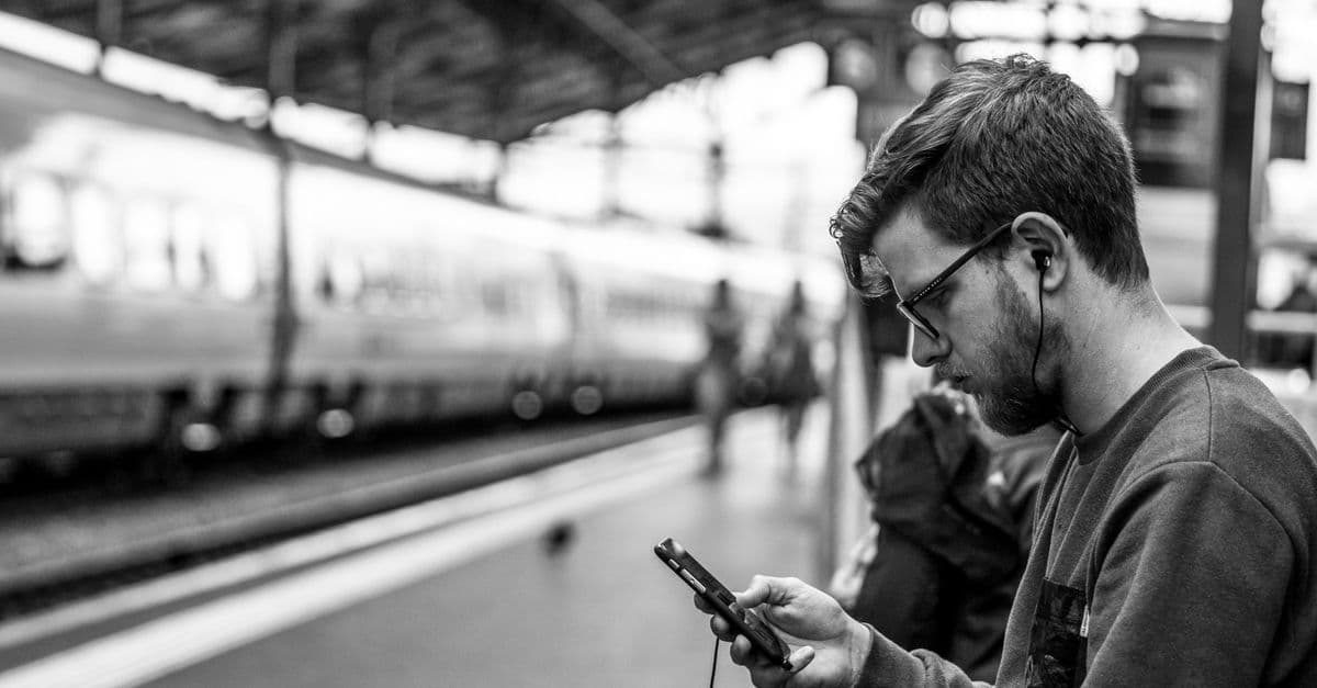 Mann mit Kopfhörern aktiviert den Swiss Travel Pass über die SBB Mobile App am Bahnhof Lausanne.