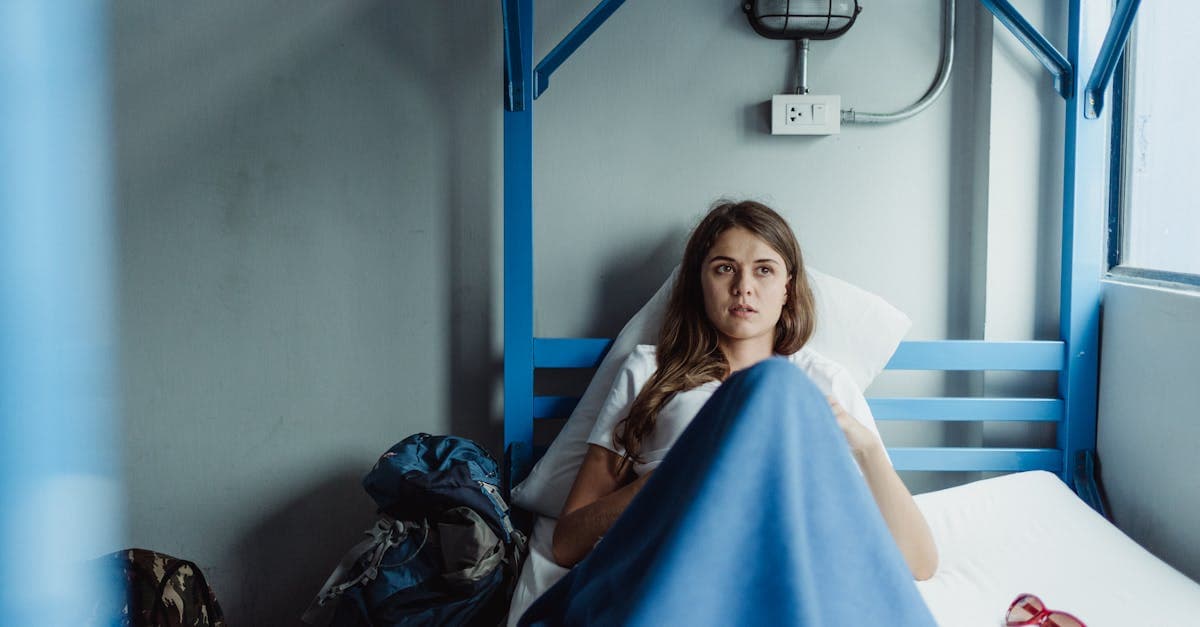 Budget-conscious solo traveller relaxing in a Japanese hostel bunk bed with backpack, glasses, and travel essentials nearby