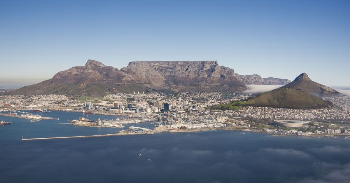 Panoramic view of Cape Town, its harbor, Table Mountain and Lion’s Head beside the ocean.