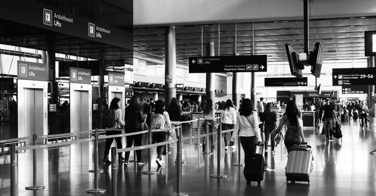 Travellers pulling luggage through a busy international airport terminal while navigating customs between connecting flights.