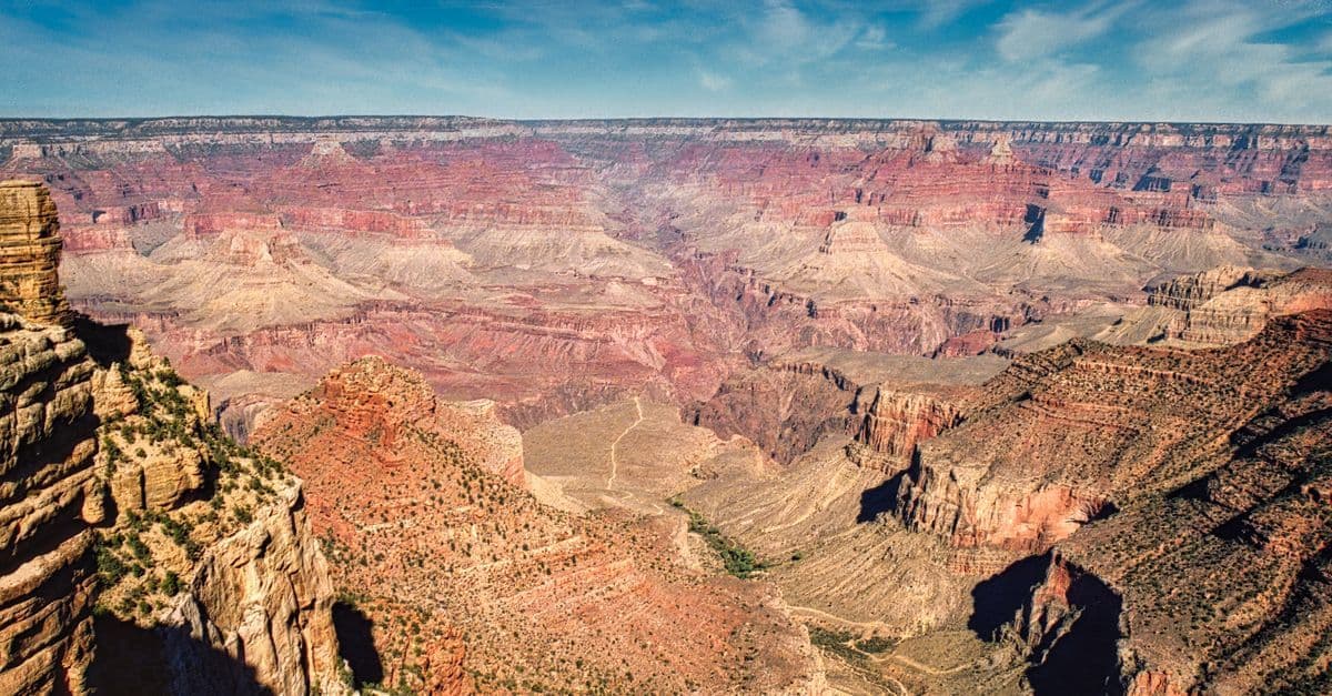 Veduta panoramica del Grand Canyon, con pareti rocciose stratificate sotto un cielo azzurro.