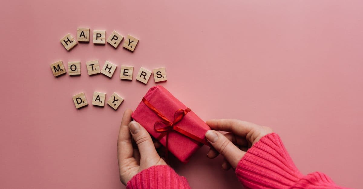 Liebevoll verpacktes Geschenk auf rosa Hintergrund symbolisiert eine Reiseüberraschung zum Muttertag.