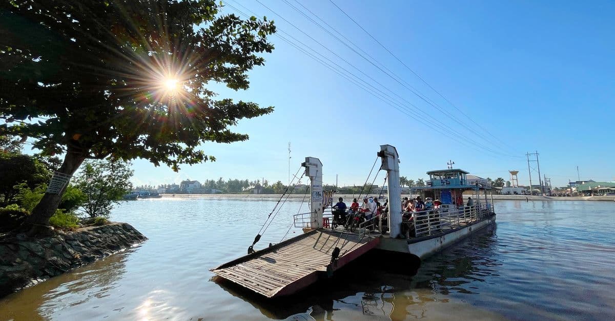 Passengers board a small ferry on a calm river beneath a sunny blue sky.