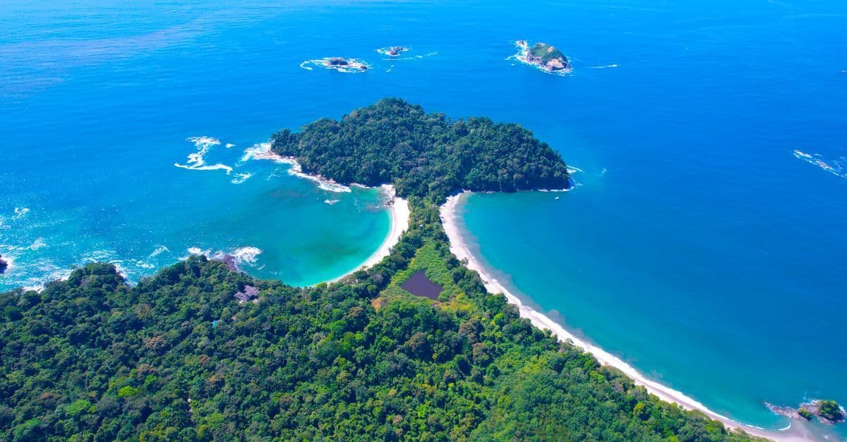 Aerial view of a lush tropical peninsula with curving white-sand beaches surrounded by bright blue ocean.