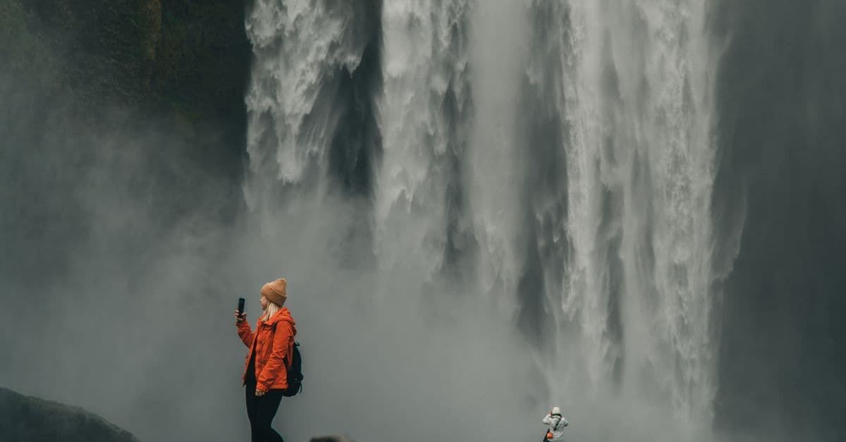 Tourists photographing Skogafoss waterfall in Iceland, exploring travel tech like android vs iphone