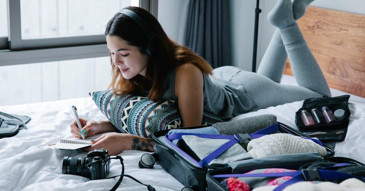 Woman writing in a notebook beside an open suitcase, building her clothing packing list.