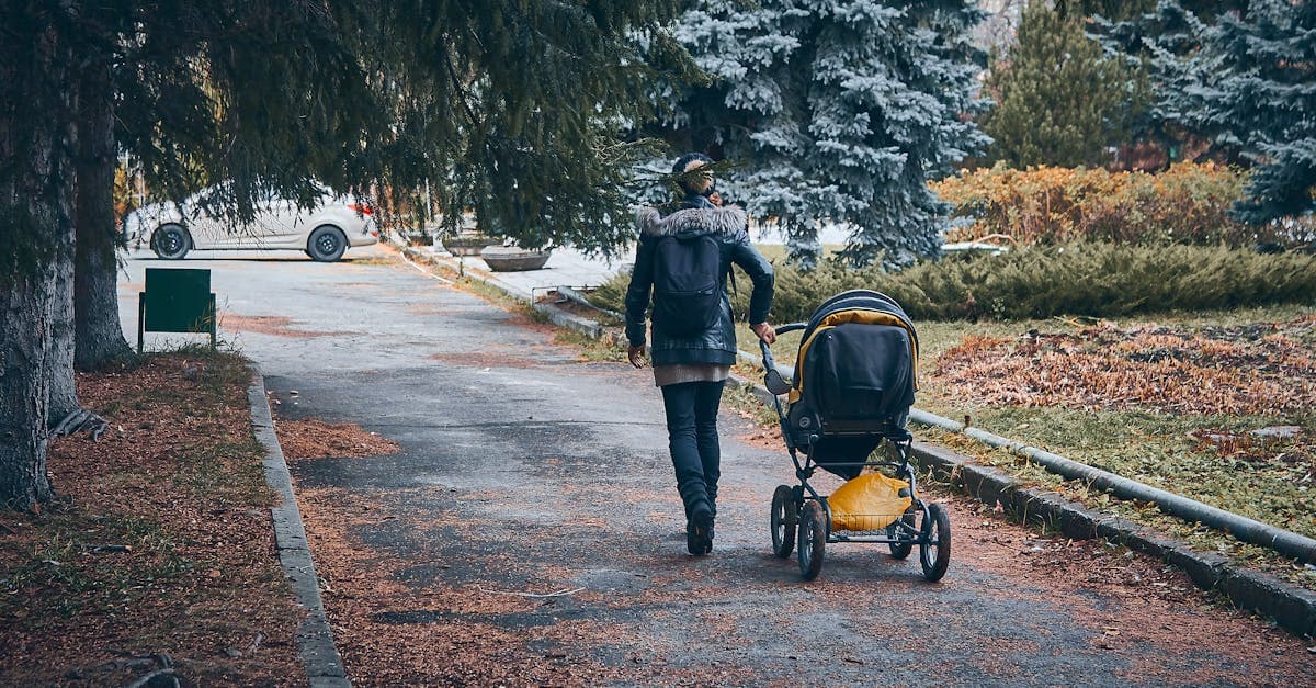 Parent pushes a travel stroller through a leafy park on a cool autumn afternoon