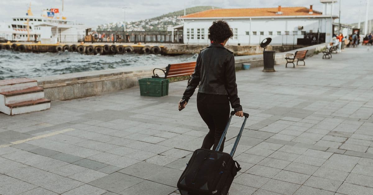 Eine Reisende zieht ihren Rollkoffer über eine Uferpromenade an einem Fähranleger in der Türkei.