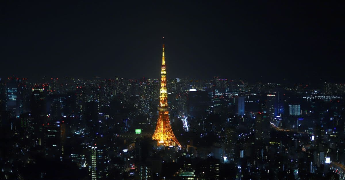 Tokio Tower rozświetlona nocą na tle panoramy metropolii Japonii.