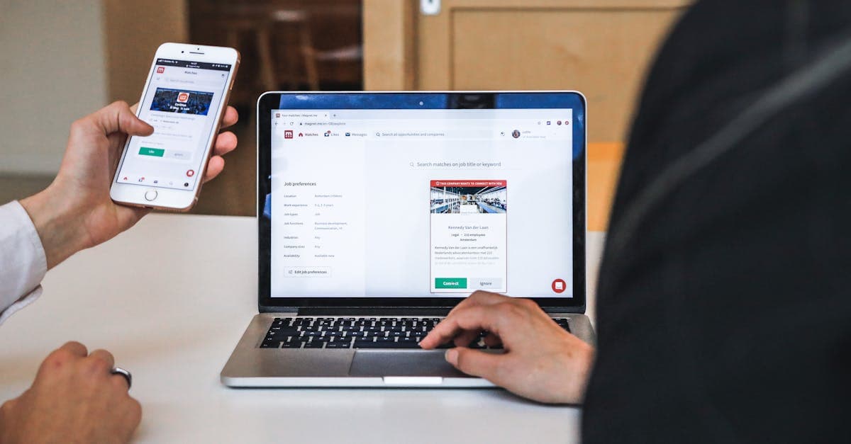 Hände bedienen Smartphone und Laptop beim Freischalten von ORF digital im modernen Büroumfeld