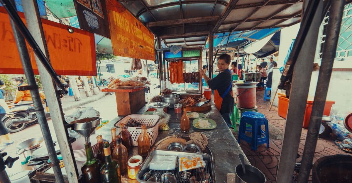 Freundlicher Streetfood-Verkäufer am Bangkoker Marktstand mit einer Vielzahl traditioneller thailändischer Gerichte