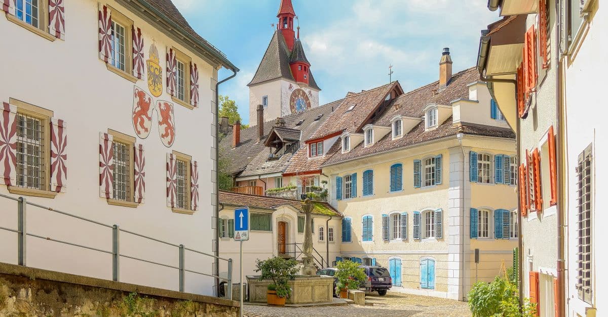 Charmante europäische Altstadtgasse mit historischen Fassaden und rotem Uhrenturm – beliebtes 12 Travel Reiseziel.