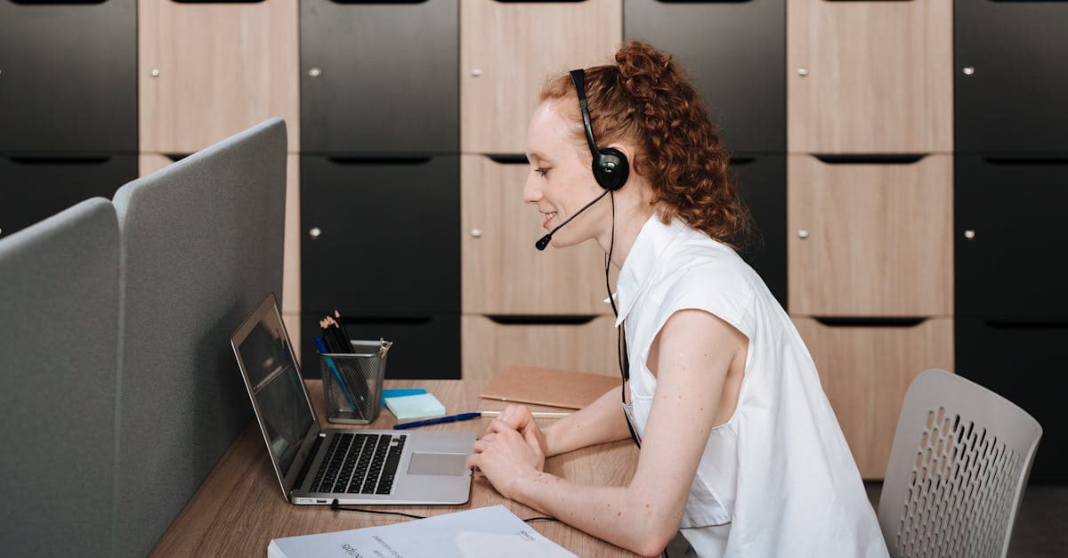 Woman wearing headset working at a laptop in a modern office environment. Ideal for telecommuting themes.