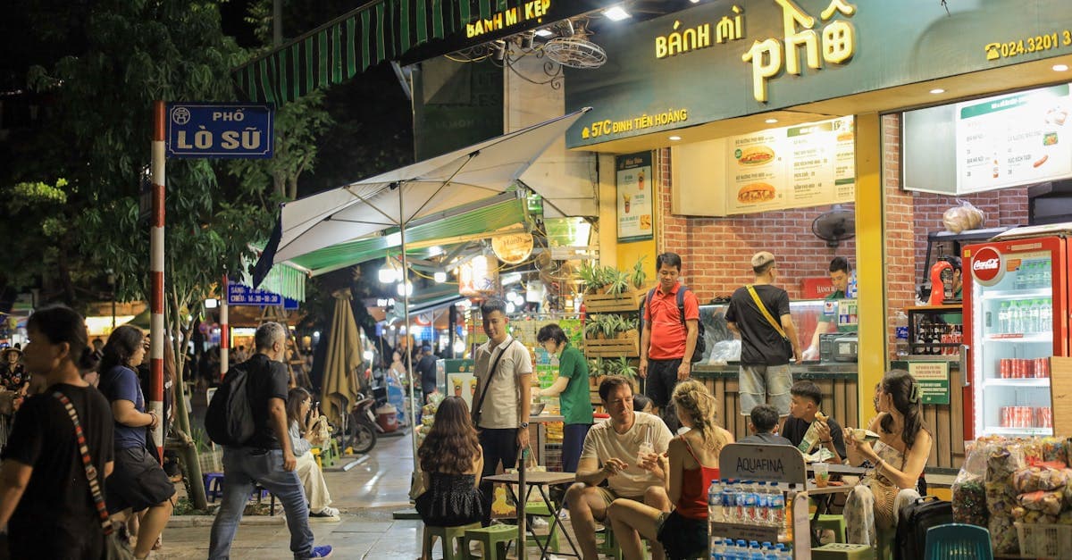 Natlig gadescene med folk der spiser banh mi og pho udenfor en vietnamesisk sandwich-bod