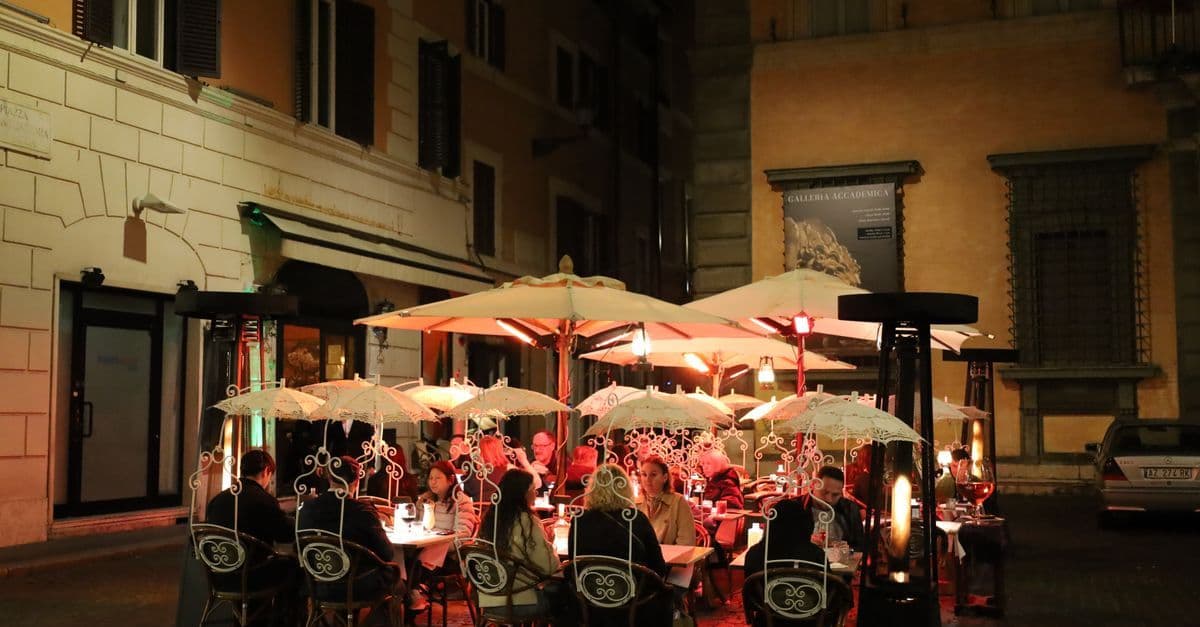Animada terraza al aire libre con sombrillas y cálida iluminación, ambiente nocturno típico de Roma.