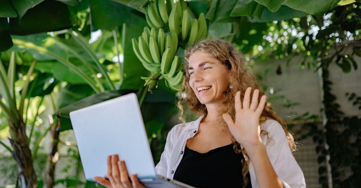 Perempuan berambut panjang video call menggunakan laptop di antara tanaman pisang tropis di Bali