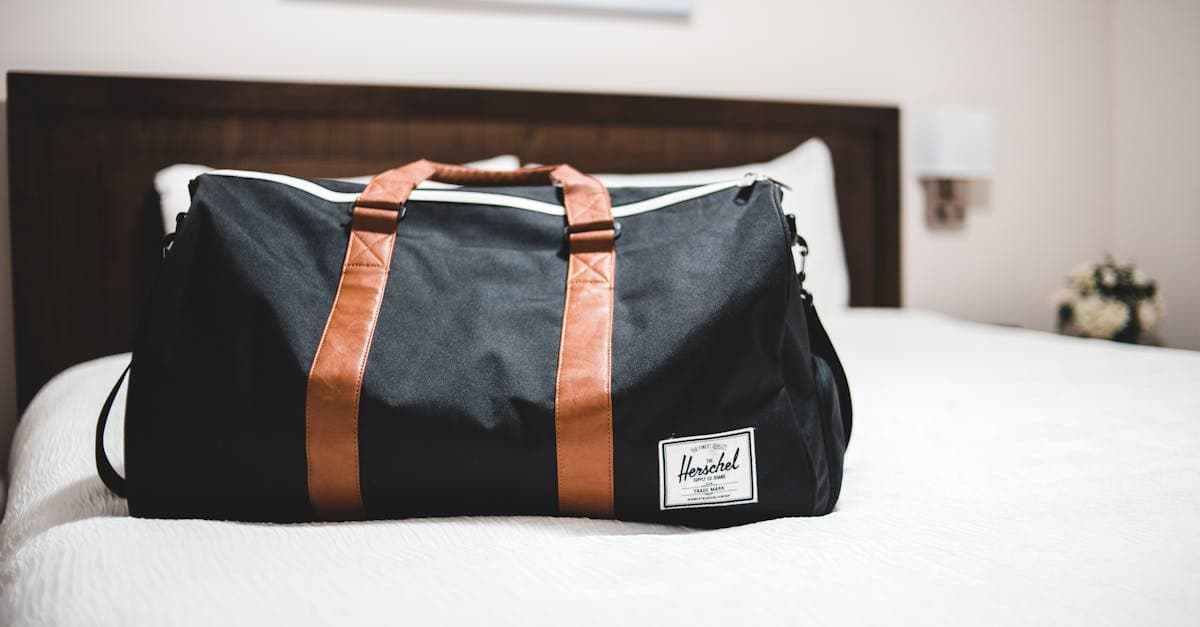 Modern travel bag med text placerad på vit sängöverkast i ett ljust hotellrum.