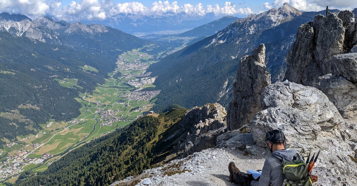 Wanderer sitzt auf einem Felsen in Tirol und genießt den Panoramablick ins Tal – Was bedeutet 'im Review'?