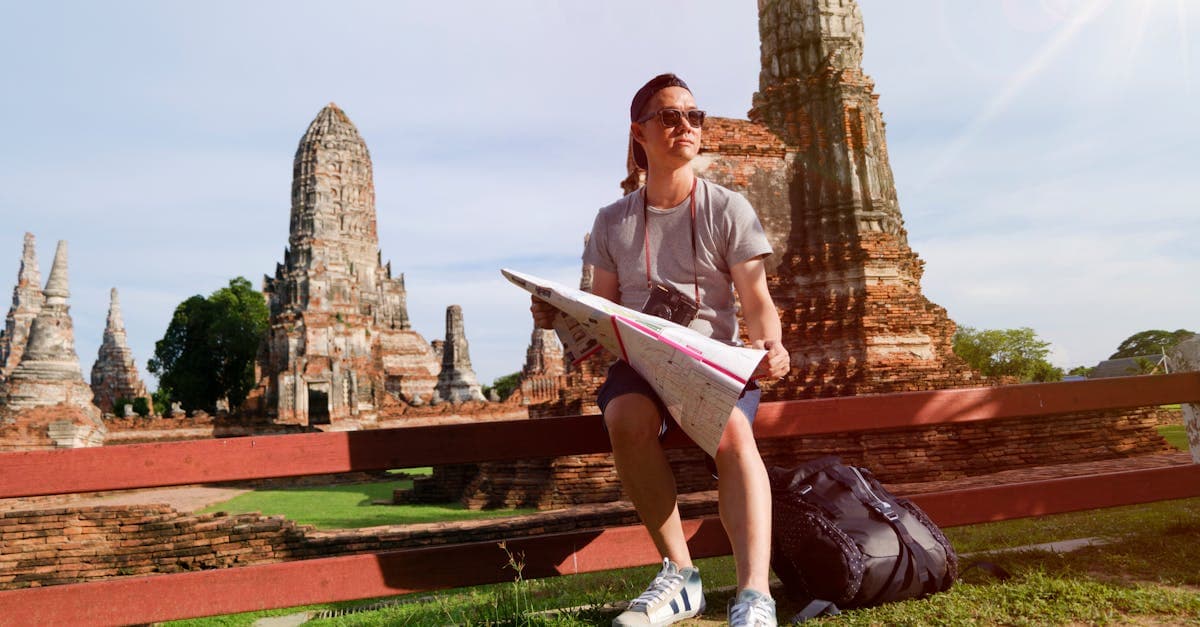 Man studying a map at ancient Thai temple ruins, planning a budget backpacking Southeast Asia trip