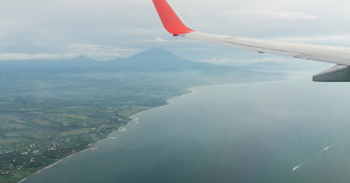 Airplane wing soaring over lush green highlands on direct flights to Bali from Australia.