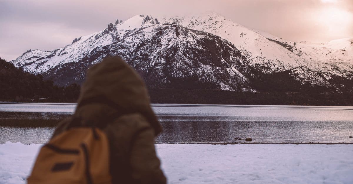 Viajante admira montanhas com neve em Bariloche às margens de um lago patagônico ao entardecer de inverno
